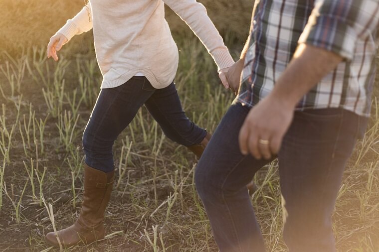 草原でブーツの女性が男性と手をつなぎながら走り出す